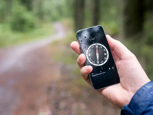 Person håller en smartphone med en digital kompassapp i en skogsmiljö