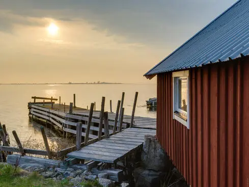 Röd stuga vid en träbrygga med solnedgång över havet i Sverige