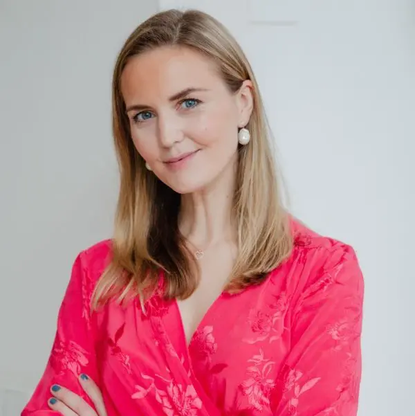 Kvinna i röd klänning med blommönster, leende och stående mot vit bakgrund